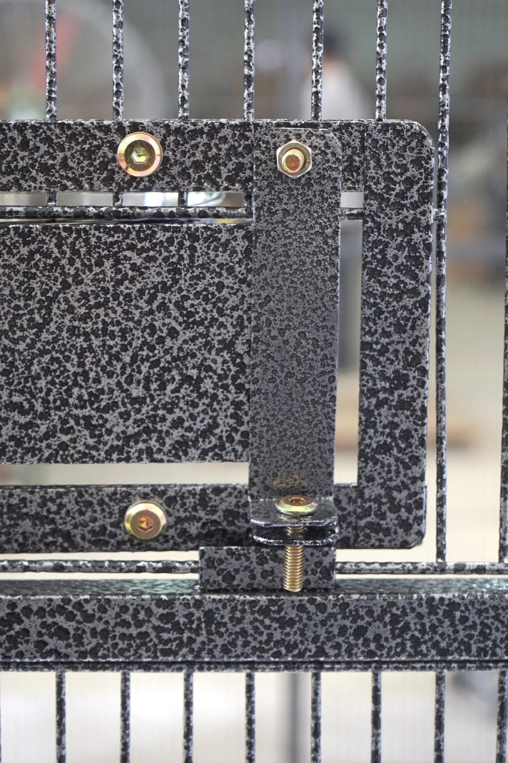 Close-up of a metal gate or enclosure with a black and gray speckled finish, featuring brass-colored mounting screws and a vertical latch bracket at Pet Servo