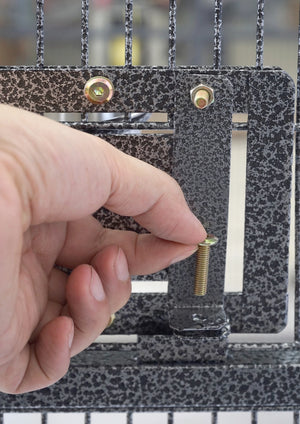 A close-up of a hand installing a brass screw into a black and white speckled metal gate or fence panel at Pet Servo