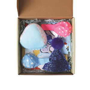 An open cardboard gift box filled with baby toys and accessories, including a light blue plush item, a pink polka-dot toy, a blue polka-dot item, a purple pom-pom, and a glittery blue item, photographed on a white background at Pet Servo