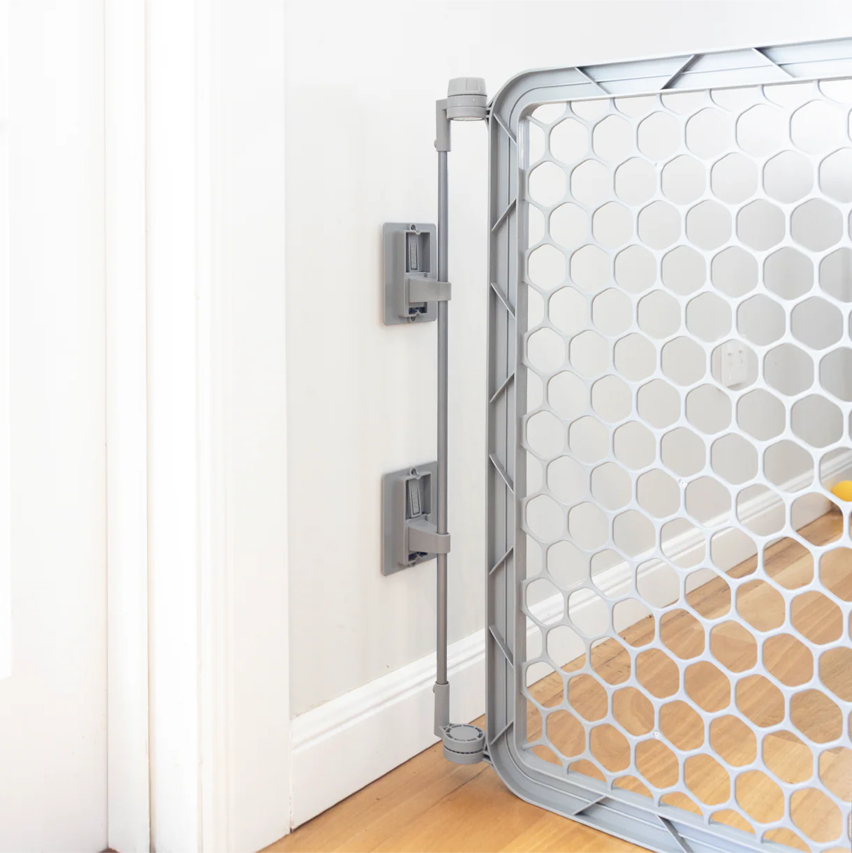 Hexagonal patterned baby gate on a wooden floor with white wall background