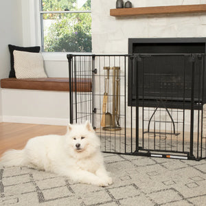 White dog lying on a rug in front of a black metal pet gate in a living room.