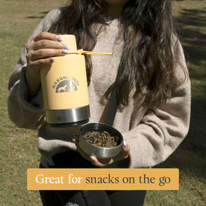 Person holding a yellow Hakuna Pet travel mug and a small bowl outdoors.