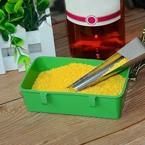 Green container with yellow beads and tongs on a wooden surface with a bottle in the background at Pet Servo