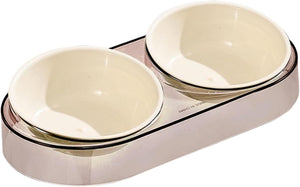 A double pet bowl set with two cream-colored ceramic bowls nested inside a sleek, metallic rose gold base, shown on a plain white background at Pet Servo