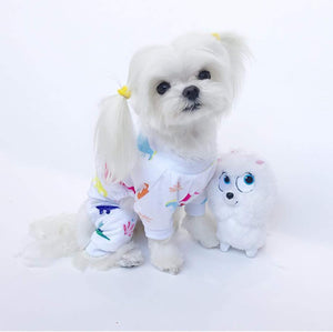 Small white dog wearing colorful pajamas with a plush toy on a light gray background at Pet Servo