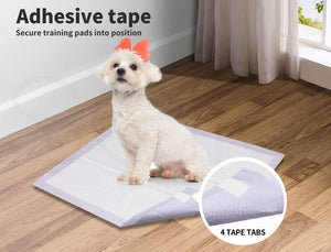 A small white dog sits on a rectangular adhesive training pad on a wood floor in a room with curtains and a window. Text at the top reads 'Adhesive tape Secure training pads into position,' and a circular inset at bottom right says '4 TAPE TABS at Pet Servo