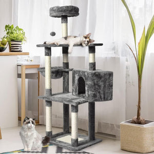 A multi-level cat tree with dark gray plush fabric and sisal-wrapped posts, shown in a bright room with two cats. One cat is lying stretched across the top platform, and other sits on the floor below at Pet Servo