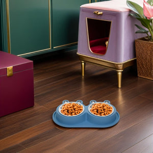 A blue dual pet feeder bowl filled with kibble sits on a dark wood floor in a styled room with a lavender pet house, green cabinets, and a magenta storage box at Pet Servo