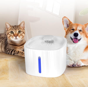 A white pet water fountain with a blue vertical indicator light, shown on a light wood floor with a tabby cat on the left and a corgi on the right at Pet Servo