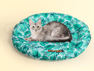 A gray tabby cat lies on a round, cushioned pet bed with a green tropical leaf pattern on a light background, set against a solid pale yellow backdrop at Pet Servo