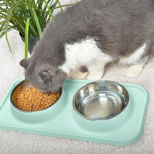 Cat eating from a metal bowl on a green pet mat with a plant in the background at Pet Servo