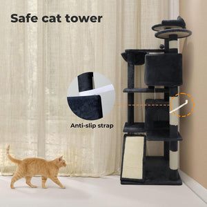 A tall black cat tower with cream-colored accents stands in a room corner beside a beige curtain. A ginger cat walks across the floor nearby, and the image includes text callouts reading 'Safe cat tower' and 'Anti-slip strap' with circular close-ups of the strap detail at Pet Servo