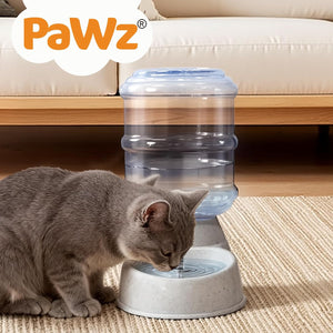 A gray cat drinking from a Pawz automatic water dispenser with a clear water bottle and white base, placed on a beige rug in front of a sofa at Pet Servo