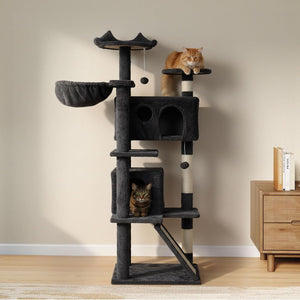 A tall dark gray cat tree with multiple platforms, a hanging bed, and two cats resting and playing on it, set in a room with a beige wall and light wood floor at Pet Servo