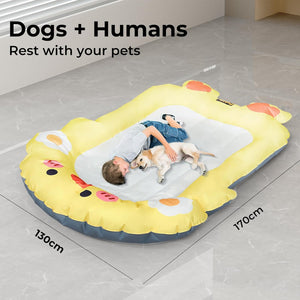 An inflatable pet bed shaped like a cartoon duck, shown with a child and a dog lying inside on a tiled floor. Text on the image reads 'Dogs + Humans Rest with your pets' with dimensions marked 130cm by 170cm at Pet Servo