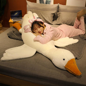 Person lying on a large goose-shaped pillow on a bed with a laptop in the background at Pet Servo