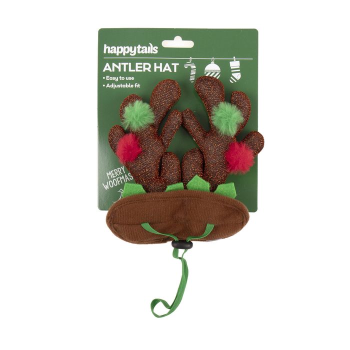 A pet antler hat accessory in brown faux fur with green and red pom-poms, attached to a green HappyTAILS retail card, on a plain white background.