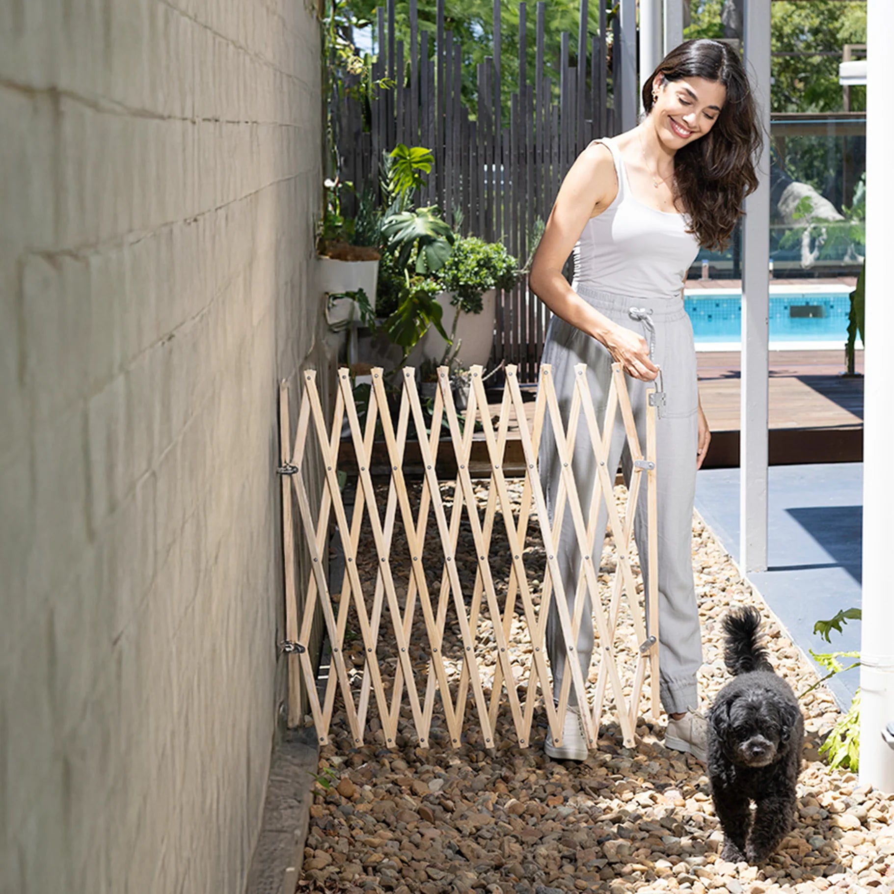 Woman opening a wooden gate in an outdoor setting with a dog nearby