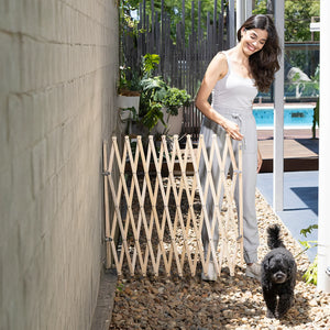 Woman opening a wooden gate in an outdoor setting with a dog nearby