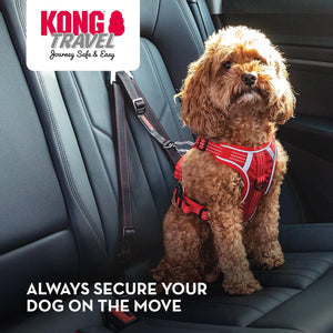 A small brown dog sits on a car seat wearing a red harness with a black leash attached. The car interior is visible, and the KONG TRAVEL logo appears in the top left with the text 'ALWAYS SECURE YOUR DOG ON THE MOVE' at the bottom at Pet Servo