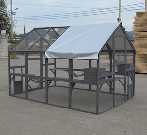 A gray metal greenhouse with a white roof cover, situated outdoors on a concrete surface with a stack of wooden boards in the background at Pet Servo