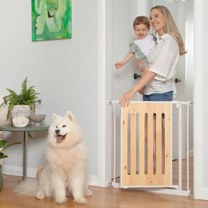 Woman holding a child next to a wooden pet gate with a dog standing on the other side.