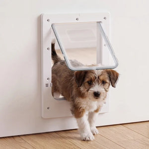 A small brown and white dog stand in front of a white pet door with a clear angled flap, set against a plain white wall and light wood floor at Pet Servo