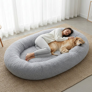 Woman and dog lying on a large gray pet bed in a room with white curtains at Pet Servo