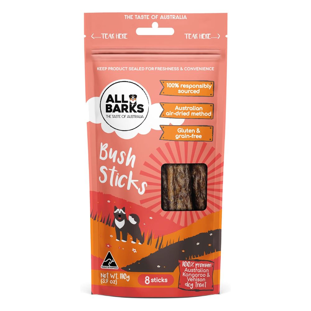 A package of All Barks Bush Sticks dog treats, featuring a resealable stand-up pouch in coral, orange, and red with illustrations of two black cats and a clear window showing the brown sticks inside.