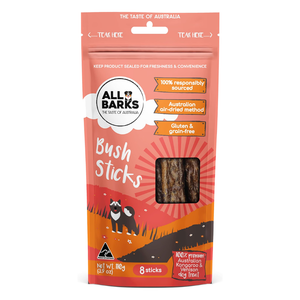 A package of All Barks Bush Sticks dog treats, featuring a resealable stand-up pouch in coral, orange, and red with illustrations of two black cats and a clear window showing the brown sticks inside.