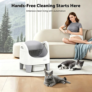A hands-free cat litter box shown in a bright living room with a woman sitting on a sofa and two gray cats on the floor. The product is white with a dark gray opening and legs at Pet Servo