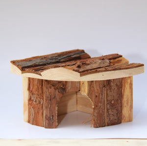 A small handmade wooden shelter or hide made from natural wood logs and bark, photographed on a plain light background at Pet Servo