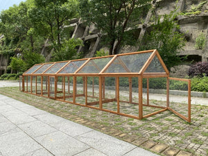 Long wooden greenhouse structure in an outdoor setting with trees and rocks in the background at Pet Servo