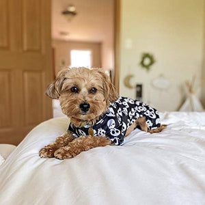 Dog wearing a black and white patterned outfit on a bed at Pet Servo