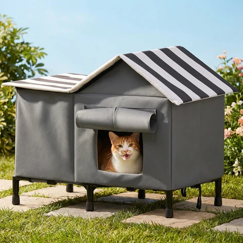 A gray outdoor cat house with a black-and-white striped roof, shown on a stone path in a garden with a cat peeking out from the front window at Pet Servo