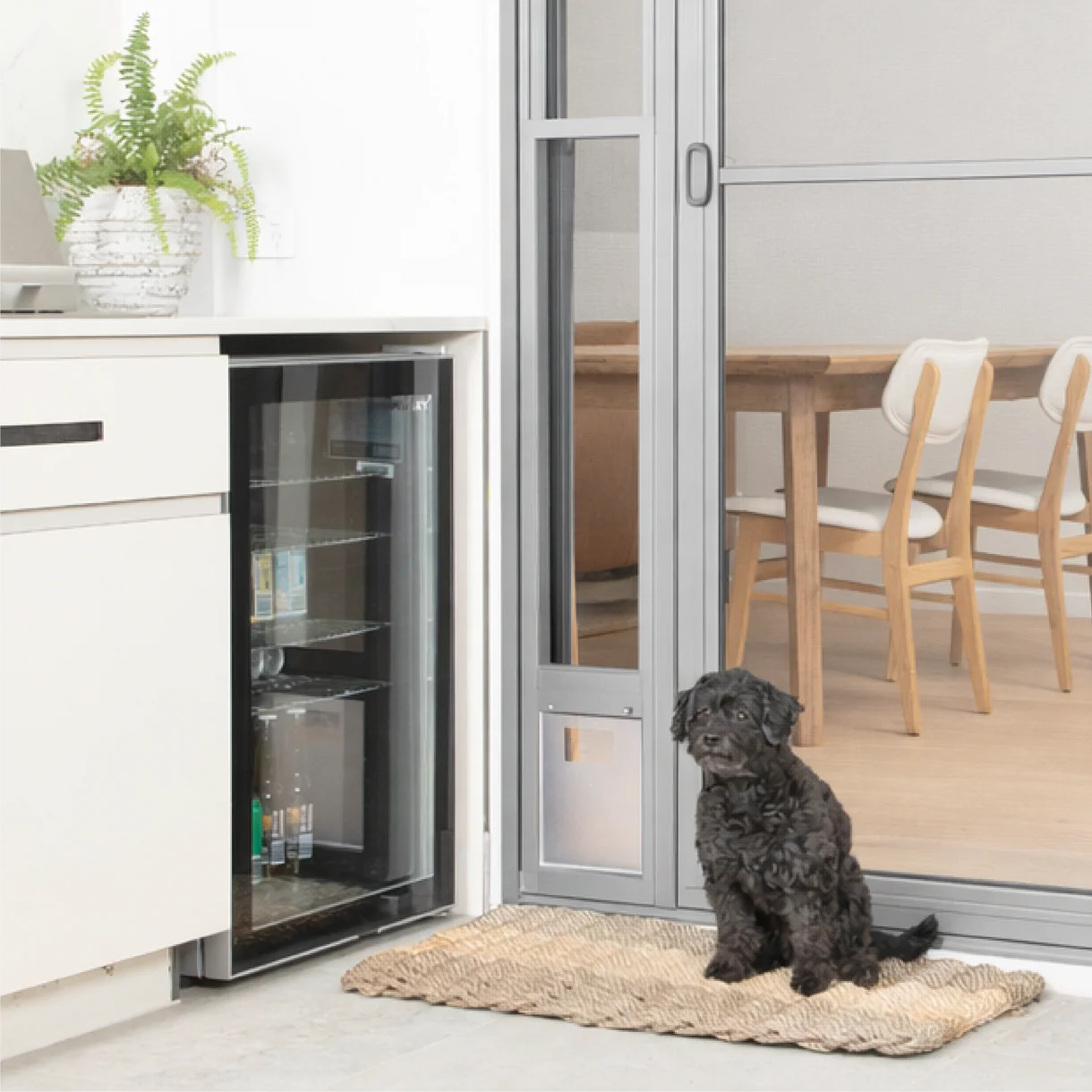 Dog sitting on a mat in front of an open refrigerator in a modern kitchen.