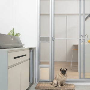 Pug dog sitting on a mat in front of a glass door with a kitchen visible inside.