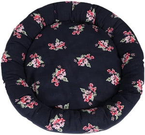 A round, plush pet bed with a dark navy blue background and a scattered pink and green floral print, shown against a plain white background at Pet Servo