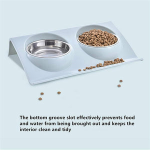 A dual-bowl pet feeder and waterer tray with stainless steel bowls, shown on a light blue background with kibble spilled on the tray. Text at the bottom explains how the bottom groove slot prevents food and water from being brought out at Pet Servo