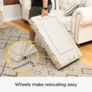 Person holding a large beige suitcase with wheels on a carpeted floor, emphasizing ease of movement.