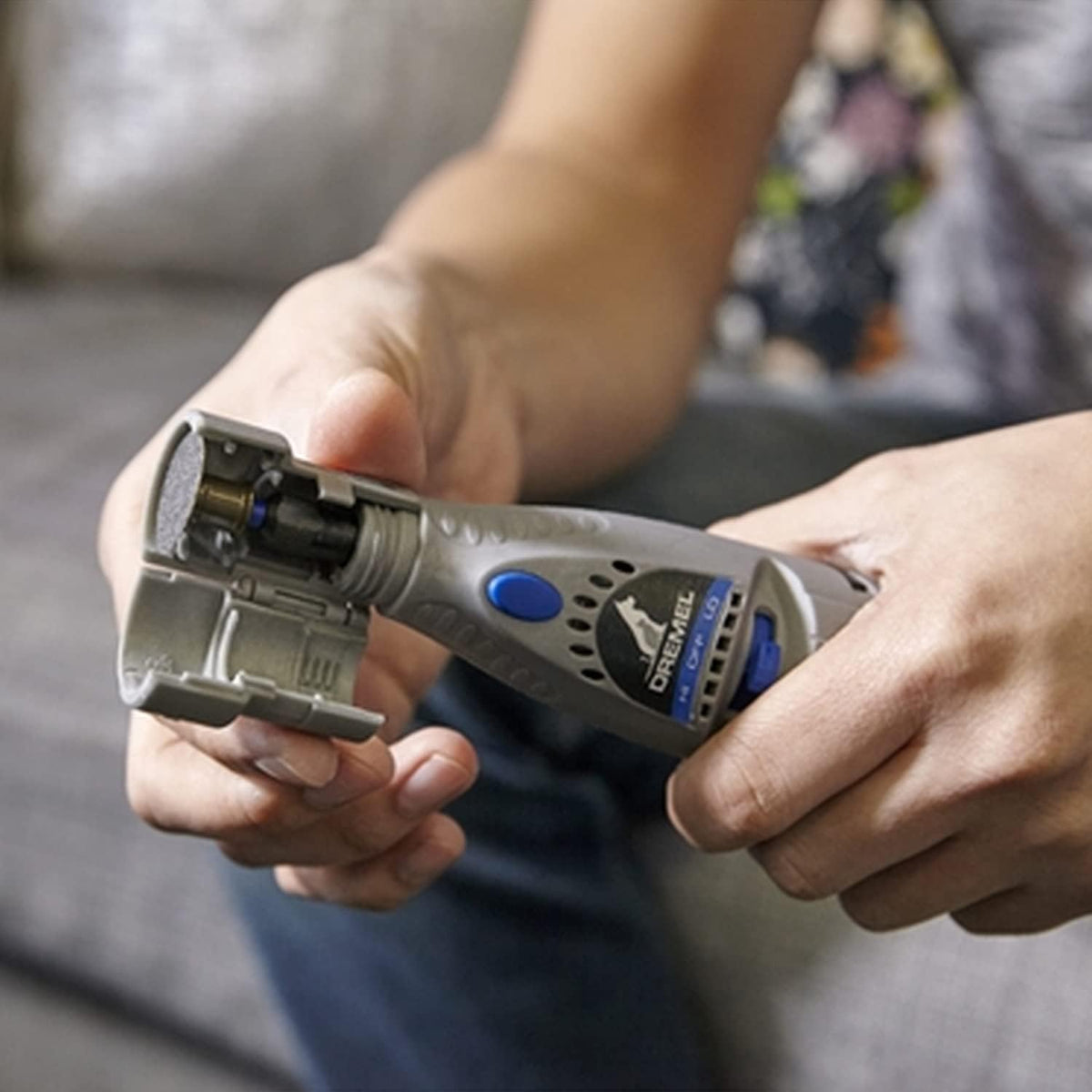 A person holding a gray and blue DeWalt rotary tool with the bit holder open, shown in a close-up shot against a blurred background.