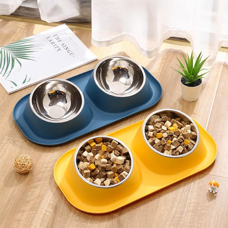 Two pet feeding trays with stainless steel bowls, one blue and one yellow, arranged on a wooden table with food in the bowls and small decorative props around them at Pet Servo
