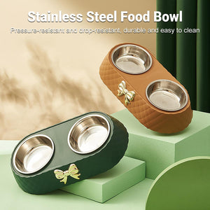 Two stainless steel double pet food bowls with quilted holders, one in dark green and one in brown, each featuring a small gold bow accent. The image includes marketing text at the top and is styled on light green display blocks at Pet Servo