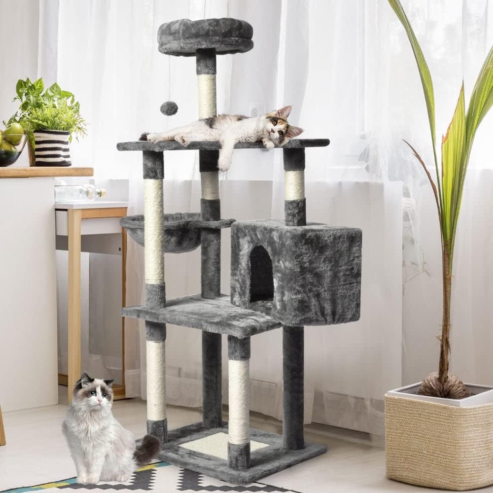 A multi-level cat tree with dark gray plush fabric and sisal-wrapped posts, shown in a bright room with two cats. One cat is lying stretched across the top platform, and other sits on the floor below at Pet Servo