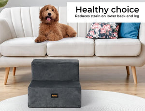 A dark gray pet step stool with a small gold 'Paws' logo, shown in front of a cream-colored sofa with a brown dog lying on it. A text banner at the top reads 'Healthy choice Reduces strain on lower back and leg' at Pet Servo