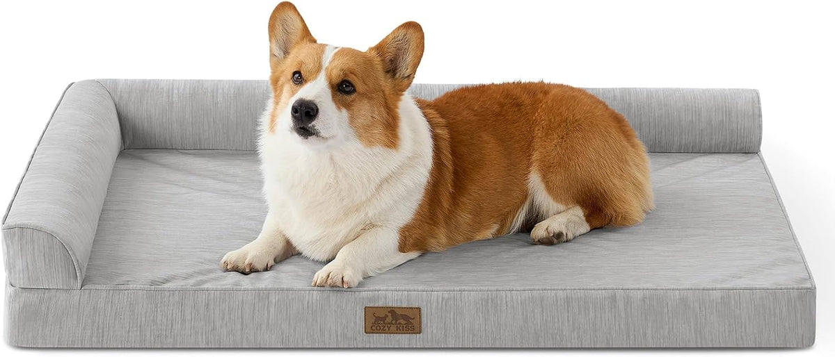 A corgi dog lies on a rectangular light gray pet bed with a raised cushioned border, photographed on a clean white background. A small brown brand patch is visible on the front edge of the bed at Pet Servo