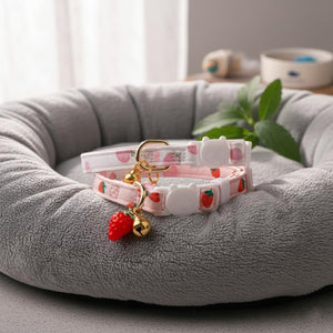 Two strawberry-themed dog collars on a gray pet bed with a plant in the background at Pet Servo
