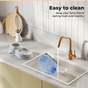A pet water bowl set shown in a kitchen setting with a marble countertop, white subway tiles, and a running faucet. The set includes a gray double bowl, a white rectangular sink tray, and a blue plastic water bottle at Pet Servo