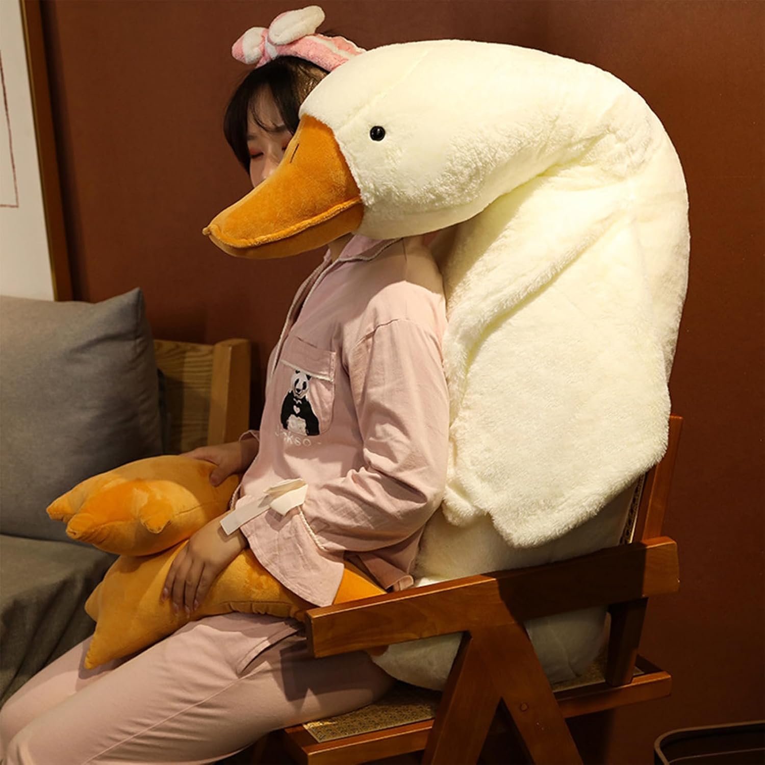 Person wearing a large plush swan headrest in a room with a brown wall at Pet Servo