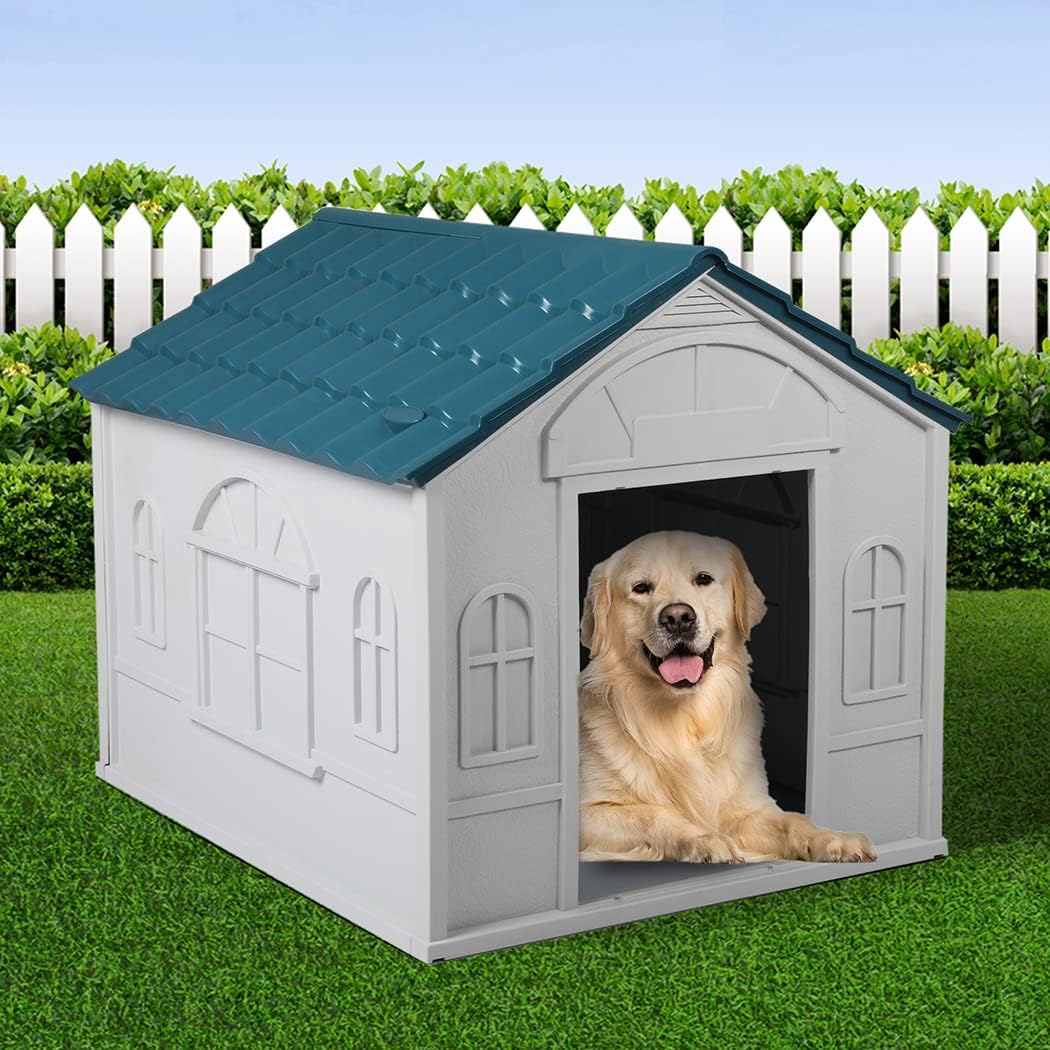 Dog sitting in a white doghouse with a blue roof on grass, white picket fence, and green bushes in the background at Pet Servo
